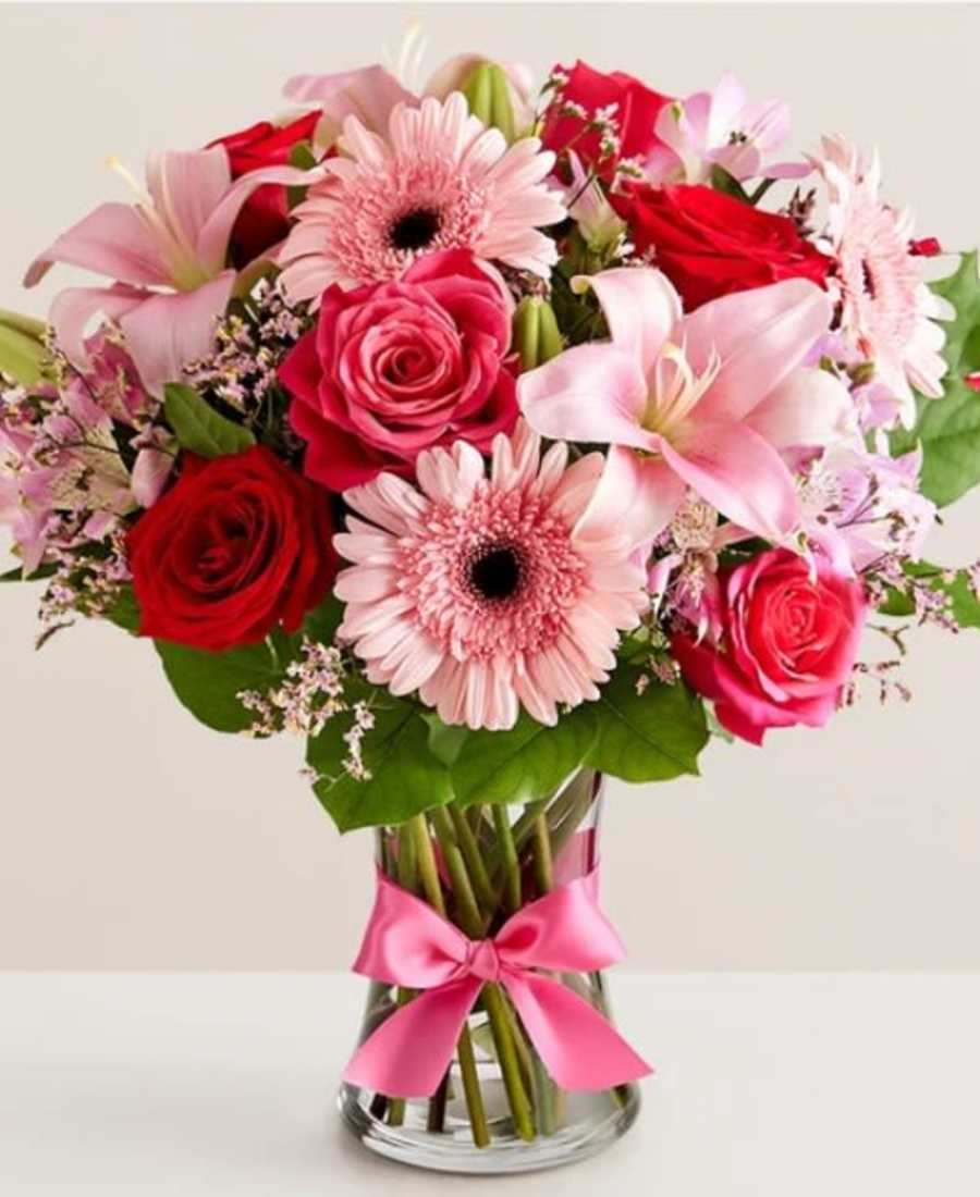 Bouquet of pink and red flowers in a clear glass vase with a pink ribbon